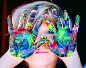 IWA Modena Family Interest Group image of a child hiding behind his hands covered in multi-coloured paint