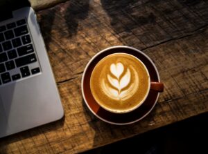 Coffee cup sat on a wooden desk next to a laptop on the left