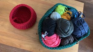 A small pink crochet basket on the left and a large overflowing blue crochet basket on the left full of balls of thick yarn