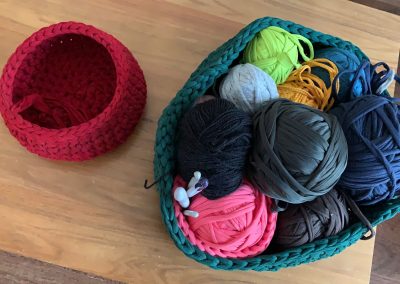 A small pink crochet basket on the left and a large overflowing blue crochet basket on the left full of balls of thick yarn
