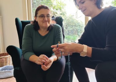 One woman showing another woman a crochet technique while sat in an armchair