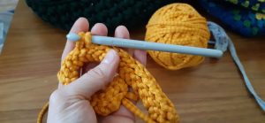 A close up of an orange yarn, crochet sample with the crochet hook in place and the ball of yarn behind