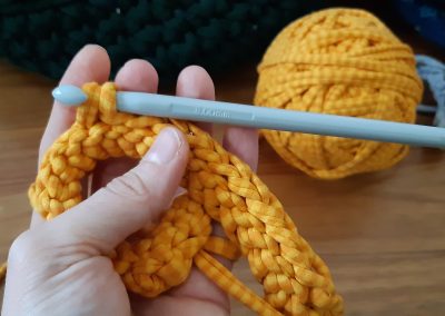 A close up of an orange yarn, crochet sample with the crochet hook in place and the ball of yarn behind